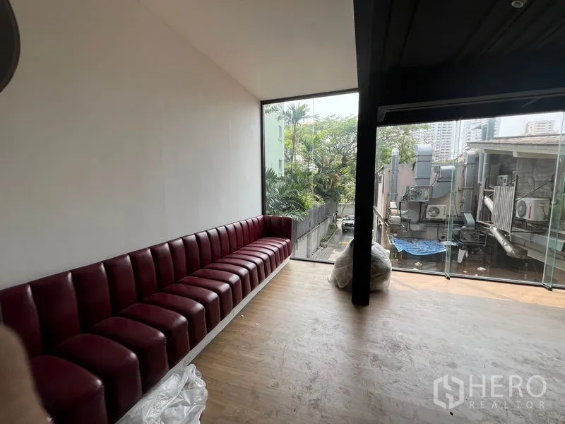 Retail Space for rent - Corner seating nook featuring a long red booth and floor-to-ceiling glass with leafy city views.