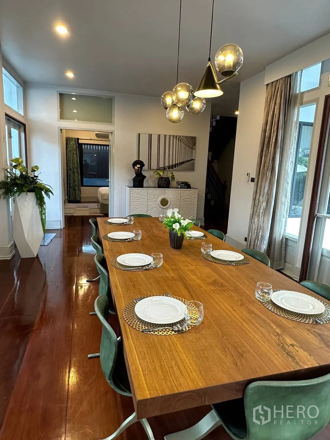 Detached House for rent in Watthana, Bangkok - Long wooden dining table set for eight with pendant lights above.