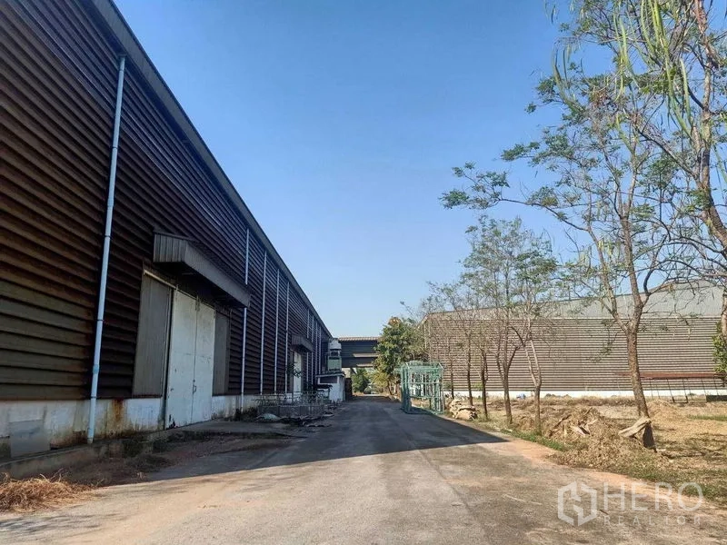 Warehouse for rent in Mueang Samut Sakhon, Samut Sakhon - Side lane beside corrugated warehouse walls with loading doors and clear blue sky.