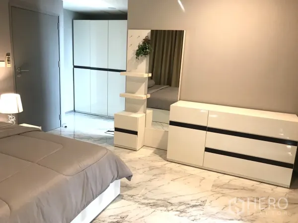 Condominium for rent in Khlong Toei, Bangkok - Modern bedroom corner with dresser, large mirror and white storage cabinets.