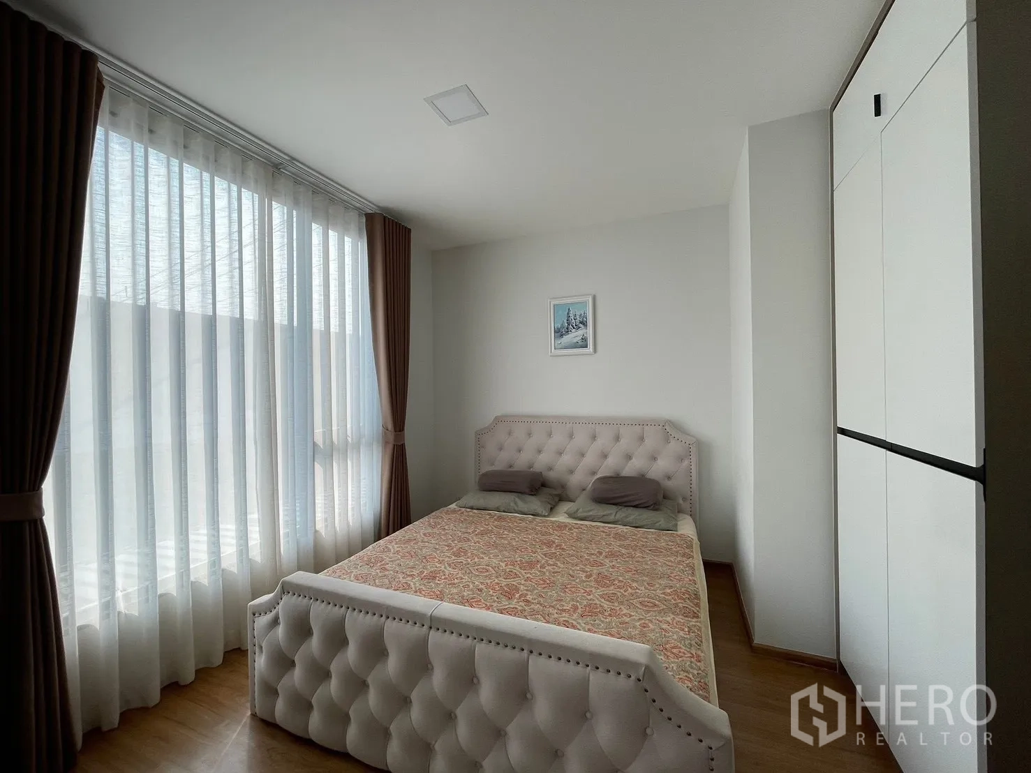 Townhouse for rent in Bang Phli, Samut Prakan - Sunlit master bedroom with a tufted bed, full-height sheer curtains, and a built-in wardrobe.