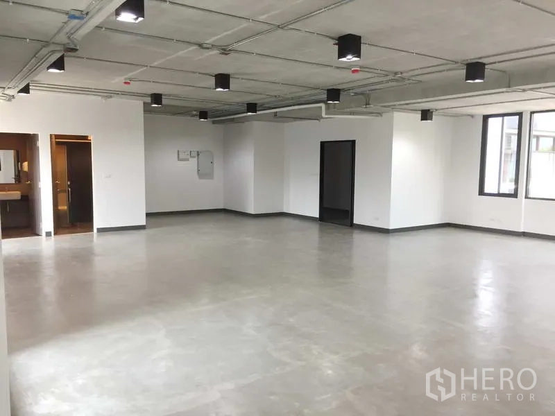 Office Space for rent in Khlong Toei, Bangkok - Spacious white-walled office with exposed ceiling lights, multiple windows and doors to restrooms.