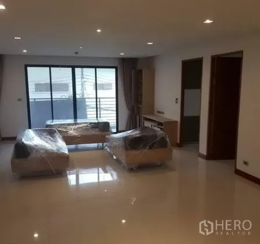 Apartment for rent in Khlong Toei, Bangkok - Spacious living area with shiny tile floors, balcony access, and new wrapped furniture.