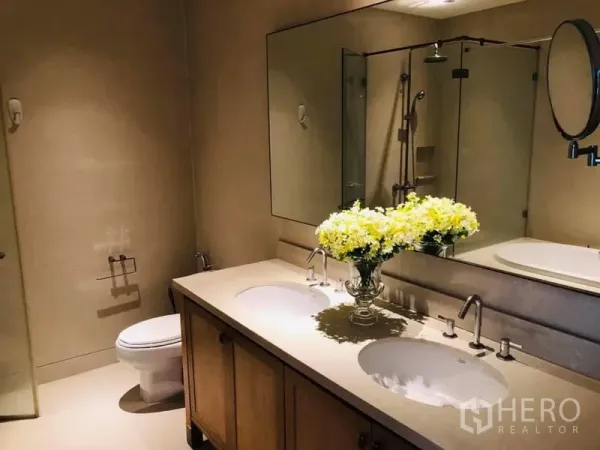 Condominium for rent in Khlong Toei, Bangkok - Spacious bathroom with double vanity, large mirror, glass shower and toilet in a Bangkok condo.