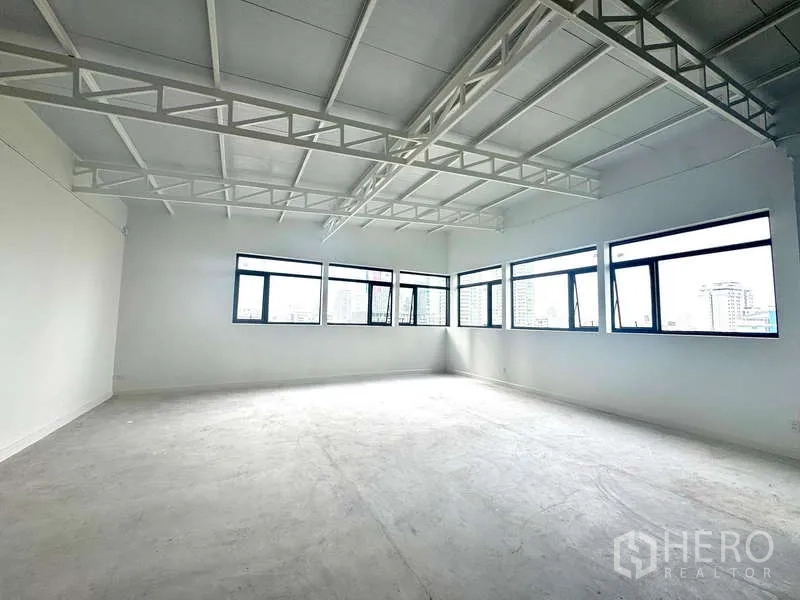 Office Space for rent in Bang Rak, Bangkok - Bright open-plan 100 sqm office with exposed truss ceiling and multiple corner windows overlooking the Bang Rak skyline.