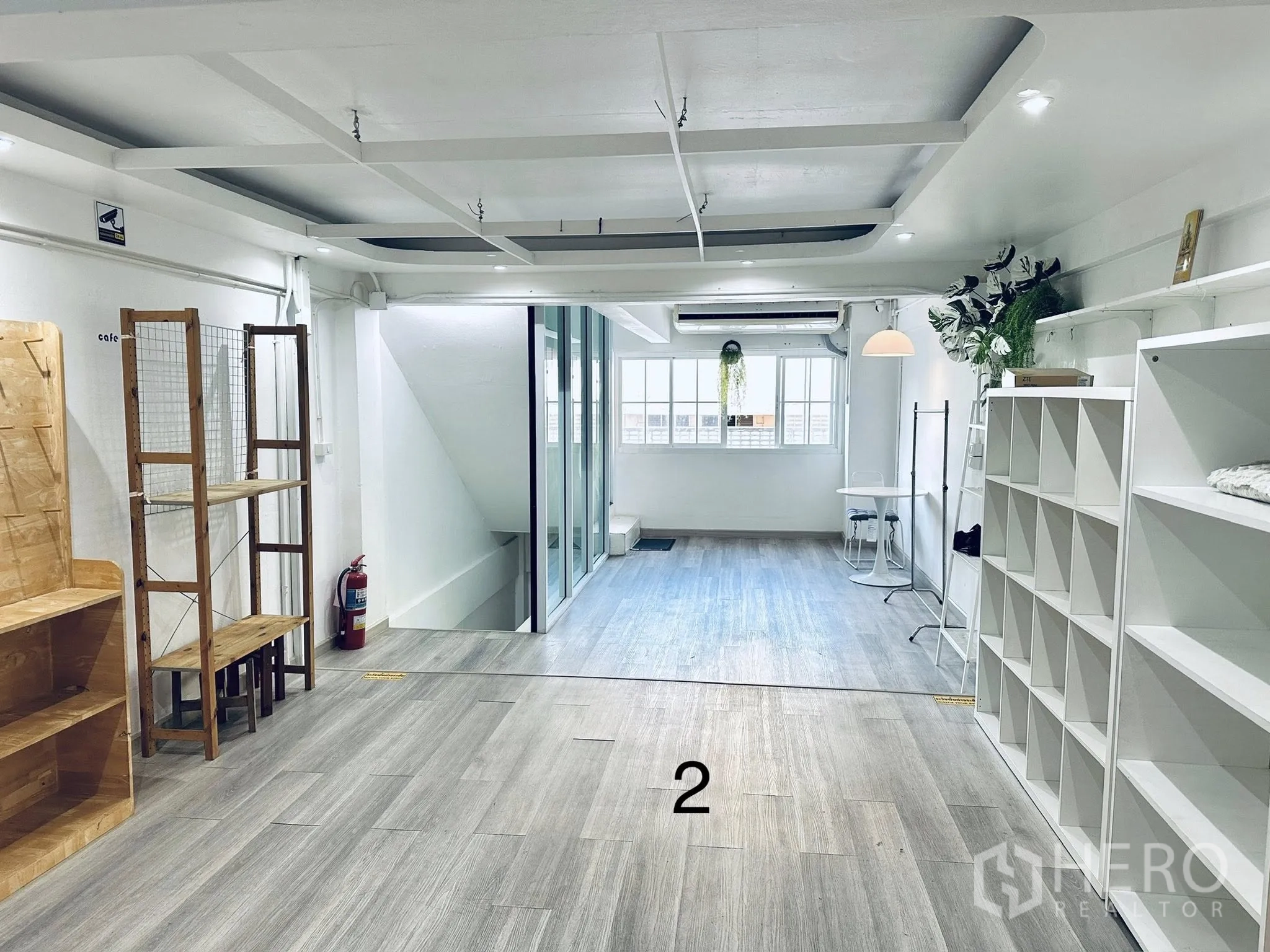 Shophouse for rent in Watthana, Bangkok - Open-plan floor with wood-look vinyl flooring, display shelves, glass partition, and windows.