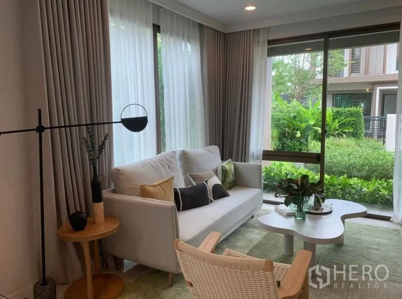 Detached House for sale in Bang Kapi, Bangkok - Bright living room with sofa, sheer curtains and large windows opening to a green garden in Bang Kapi.