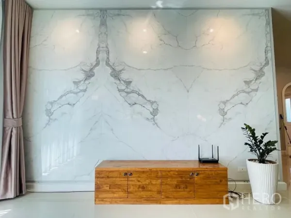 Detached House for sale in Lam Luk Ka, Pathum Thani - Living room feature wall in white marble with wooden TV console and a potted plant.