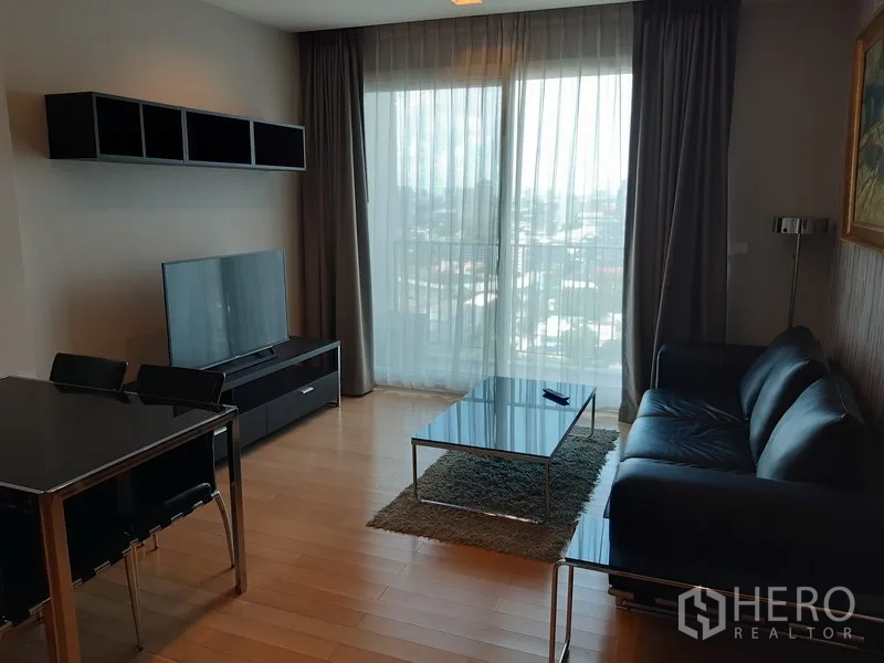 Condominium for rent in Khlong Toei, Bangkok - Bright living room with floor-to-ceiling curtains, city-view balcony, sofa, TV console, and dining set.
