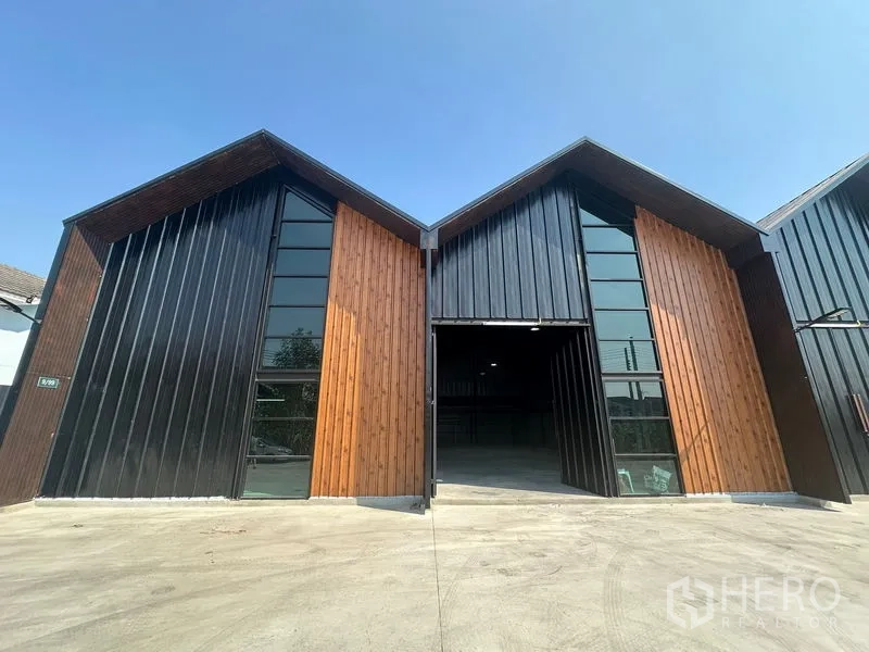 Warehouse for rent in Bueng Kum, Bangkok - Modern twin-gable warehouse exterior with black metal and wood cladding and a wide driveway in Bueng Kum, Bangkok.