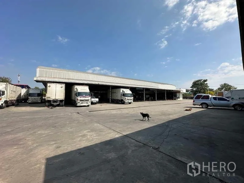 Warehouse for rent in Lam Luk Ka, Pathum Thani - Wide yard facing the main loading bays with trucks and cars parked.