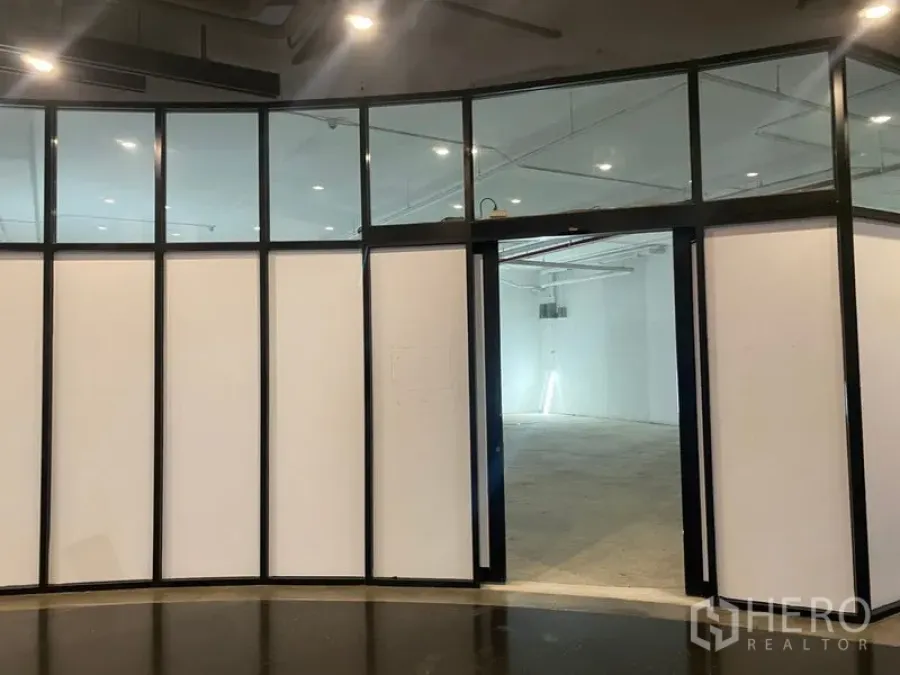 Retail Space for rent - Curved black‑framed glass storefront opening to a white‑shell retail unit with ceiling spotlights.