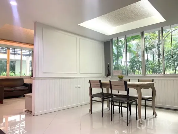 Condominium for rent in Khlong Toei, Bangkok - Dining area with wooden table, ceiling light and large windows facing lush garden view.