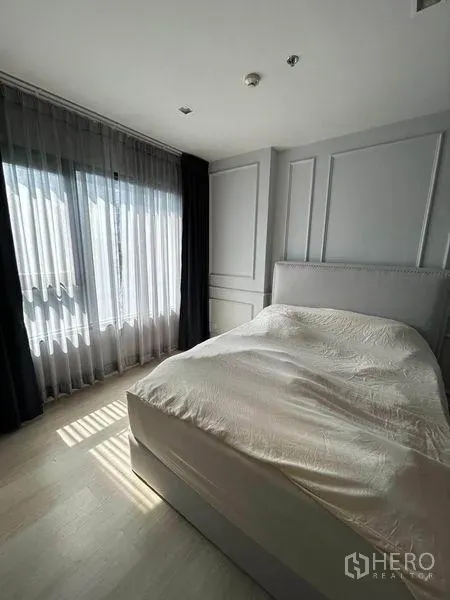 Condominium for sale in Pathum Wan, Bangkok - Cozy one‑bedroom interior featuring light wood flooring, tall windows with layered curtains, and a soft gray palette.
