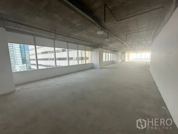 Office Space for rent in Watthana, Bangkok - Long workspace with rows of windows on both sides, raw concrete ceiling with ducts, bright natural light at each end.