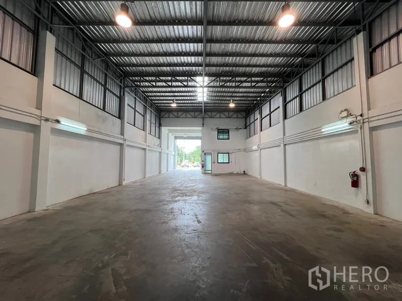 Warehouse for rent in Bang Phli, Samut Prakan - Warehouse interior facing the loading entrance, high ceilings, lighting and a small office box.