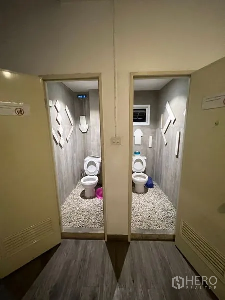 Shophouse for rent or sale in Watthana, Bangkok - Two separate toilet stalls with grey finishes and pebble‑stone flooring.