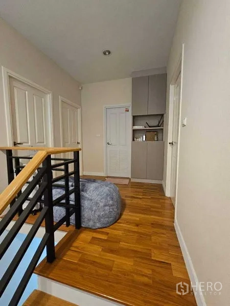 Detached House for sale in Khan Na Yao, Bangkok - Upstairs landing with wooden flooring, black handrail, built-in cabinet and multiple doors.