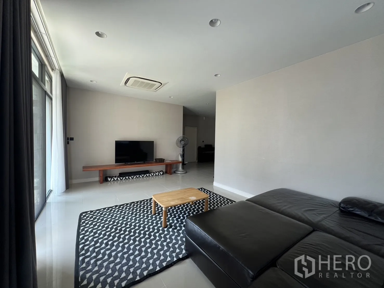 Detached House for rent or sale in Bang Kapi, Bangkok - Minimalist lounge with TV console, patterned rug and sectional sofa.