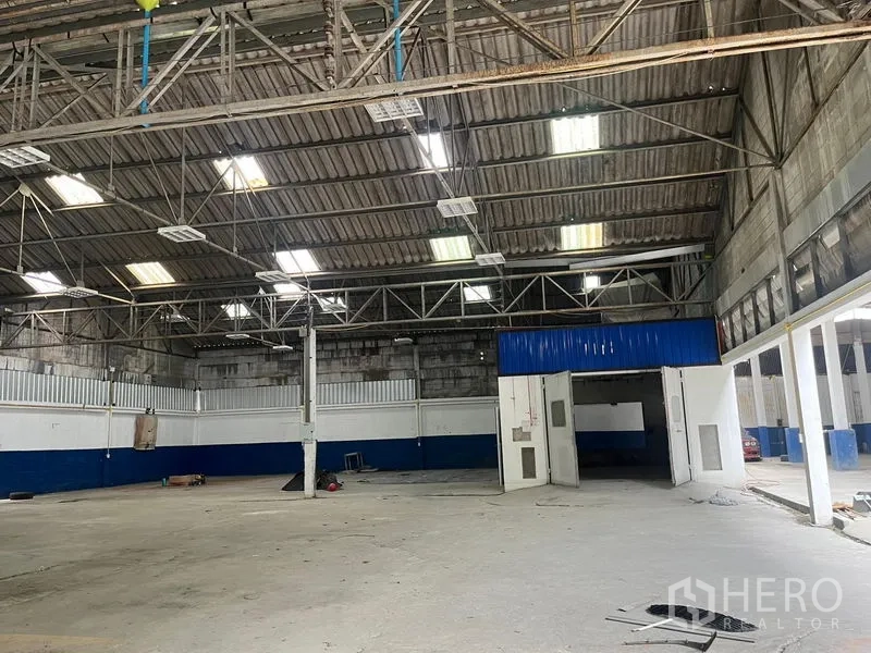 Warehouse for rent in Phra Khanong, Bangkok - Interior view with truss roof, bright lighting, and large double doors to ancillary rooms.