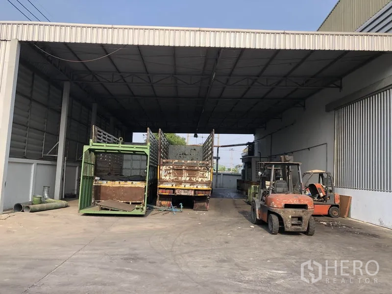 Factory for rent in Bang Bua Thong, Nonthaburi - Covered loading bay with high metal roof, forklifts and trucks positioned for goods handling.