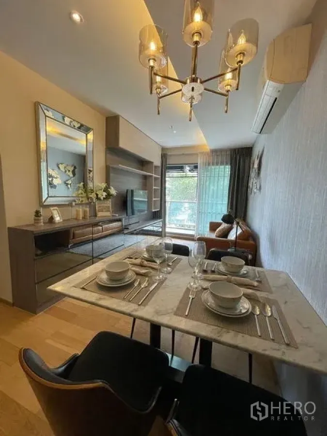 Condominium for rent in Watthana, Bangkok - Dining space with marble table set for four, chandelier, TV cabinet, and view to the balcony.
