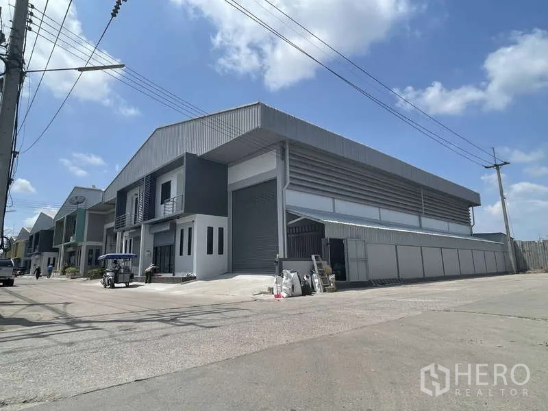 Factory for rent in Ban Phaeo, Samut Sakhon - Corner street view of the warehouse complex with big roller shutter and wide road access.