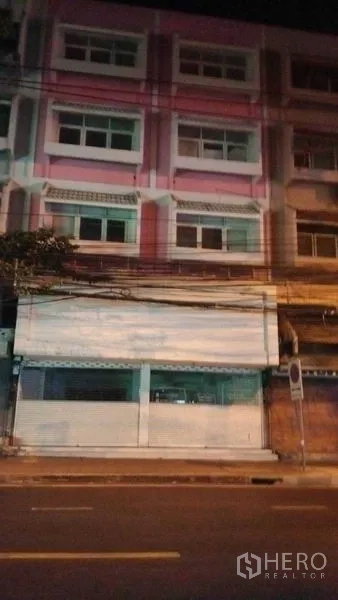Shophouse for rent in Watthana, Bangkok - Four-storey shophouse exterior with shuttered ground-floor shopfront at night.