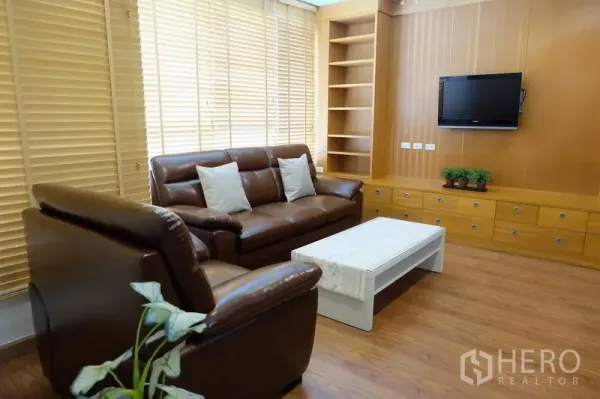 Condominium for rent in Khlong Toei, Bangkok - Cozy living room featuring brown leather sofa, TV, built-in cabinetry and coffee table