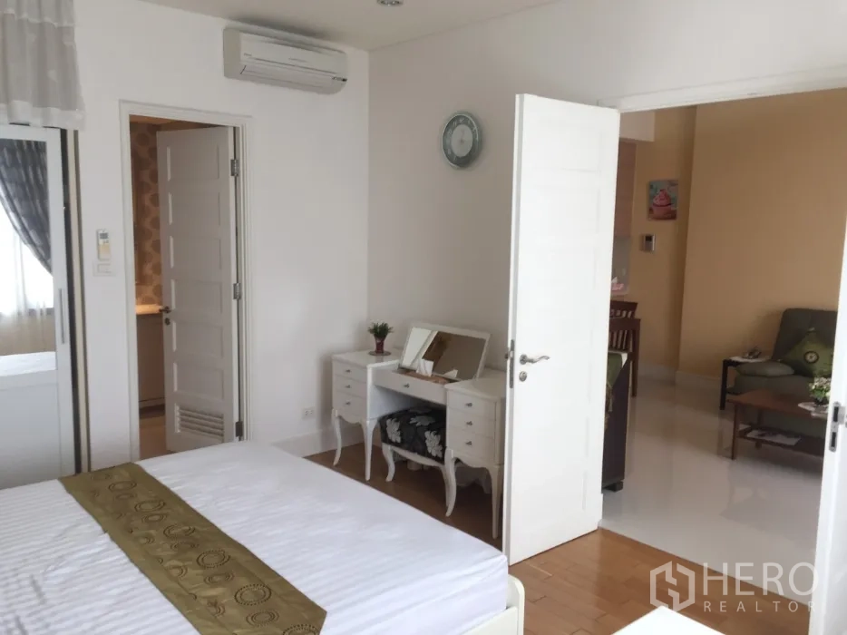 Condominium for rent or sale in Khlong Toei, Bangkok - Bedroom view showing dressing table, air conditioner and wood flooring leading to the living area.
