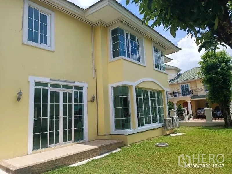 Detached House for sale in Prawet, Bangkok - Rear facade with large bay windows opening to a green lawn garden.