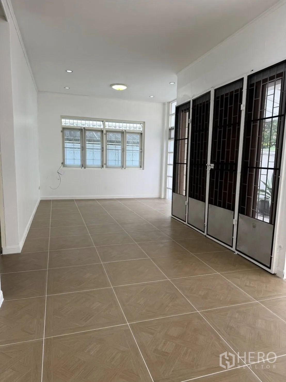 Detached House for rent in Khlong Toei, Bangkok - Spacious living area with large windows, tiled floors, and metal-grilled doors.