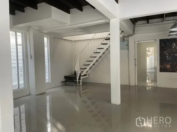 Detached House for rent in Huai Khwang, Bangkok - Open-plan living area with glossy floors, exposed beams and a white metal staircase.