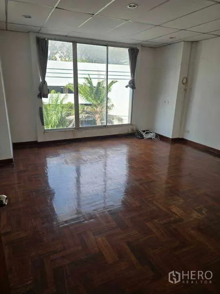 Shophouse for rent in Watthana, Bangkok - Top-floor room with wide window and tree views, polished parquet flooring.