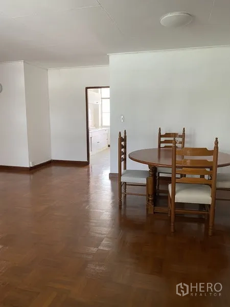 Apartment for rent in Khlong Toei, Bangkok - Dining corner with wooden round table and chairs next to doorway leading to a bright kitchen.