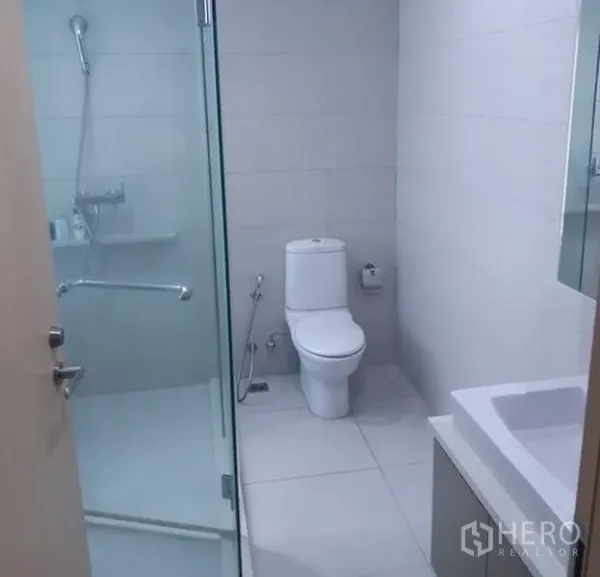 Condominium for rent in Khlong Toei, Bangkok - Bright bathroom with glass-enclosed shower, white tiles and modern toilet.