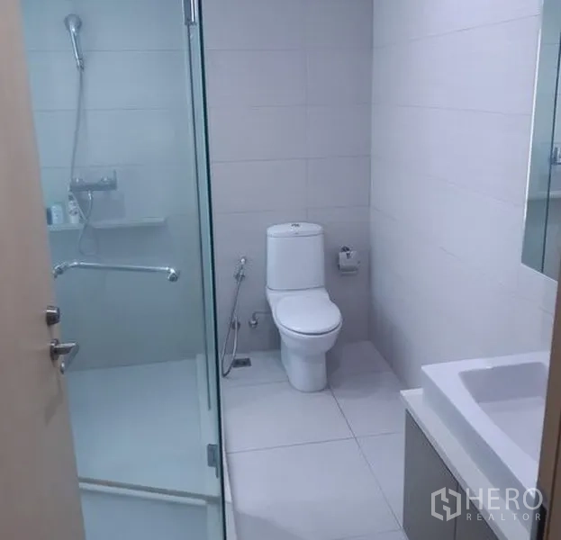 Condominium for rent in Khlong Toei, Bangkok - Bright bathroom with glass-enclosed shower, white tiles and modern toilet.