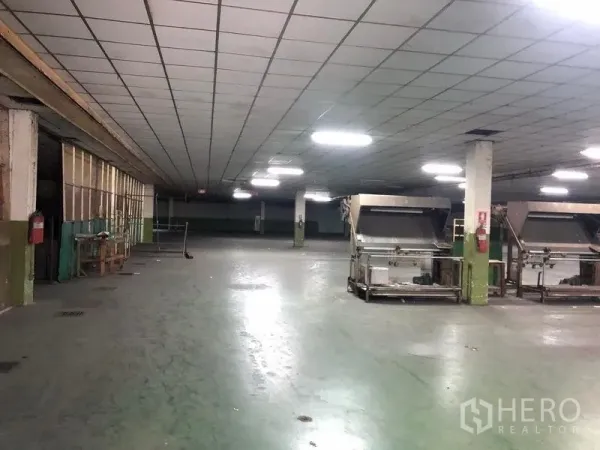 Factory for rent in Lat Krabang, Bangkok - Spacious production hall with columns, bright ceiling lights and industrial machines on a concrete floor.