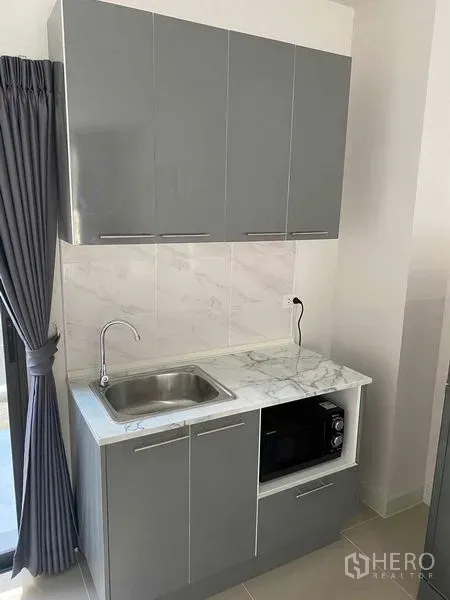 Townhouse for rent in Prawet, Bangkok - Compact grey kitchenette with marble countertop, sink and microwave in a modern Bangkok townhouse.