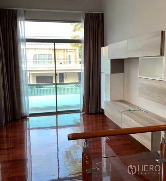Detached House for sale in Mueang Pathum Thani, Pathum Thani - Upstairs family area with sliding glass door to a balcony, built-in wall cabinet and wood floors.