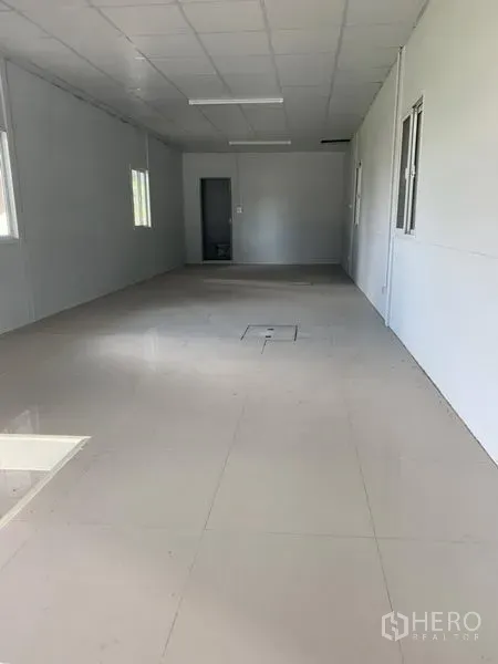 Factory for rent in Khlong Luang, Pathum Thani - Clean office room with tiled floors, white walls, suspended ceiling, windows, and a door leading to the bathroom.