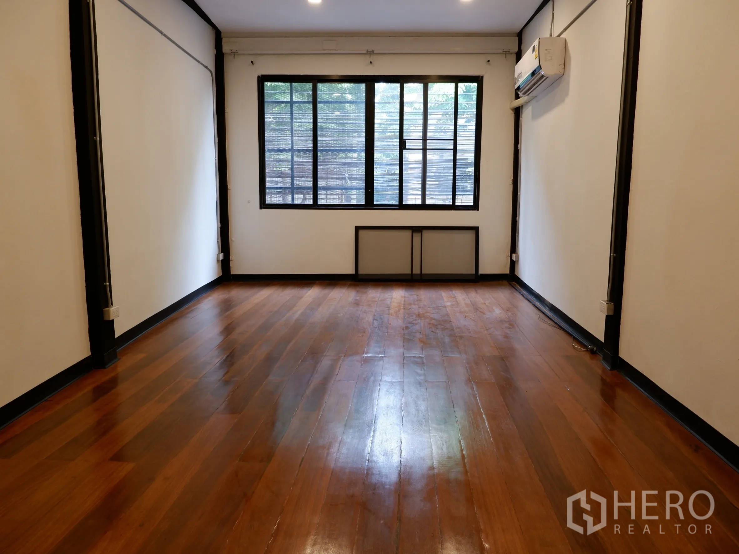Home Office for sale in Bang Rak, Bangkok - Spacious room with polished wooden flooring, large window and wall-mounted air conditioner.