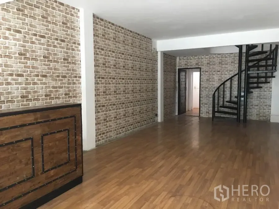 Shophouse for rent in Khlong Toei, Bangkok - Open-plan shophouse interior with brick feature walls, wood flooring, a wooden counter, and a black spiral staircase.
