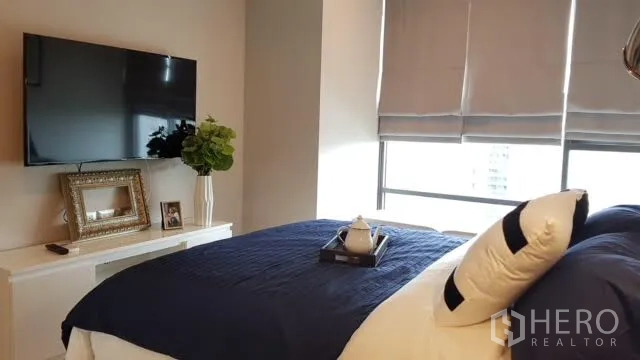 Condominium for rent in Khlong Toei, Bangkok - Bedroom with wall-mounted TV, large window with blinds and a console cabinet.