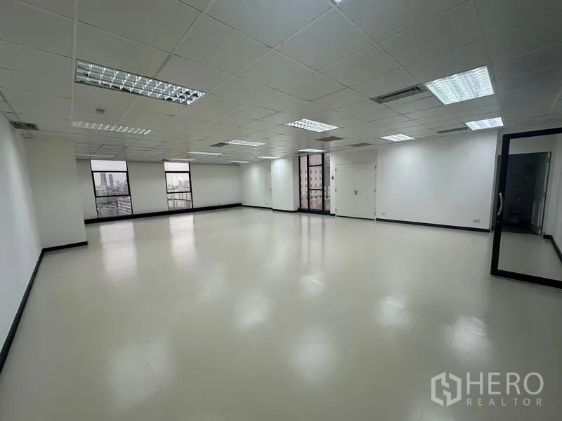 Office Space for rent - Spacious empty office floor with multiple windows, clean flooring, glass door and suspended ceiling.