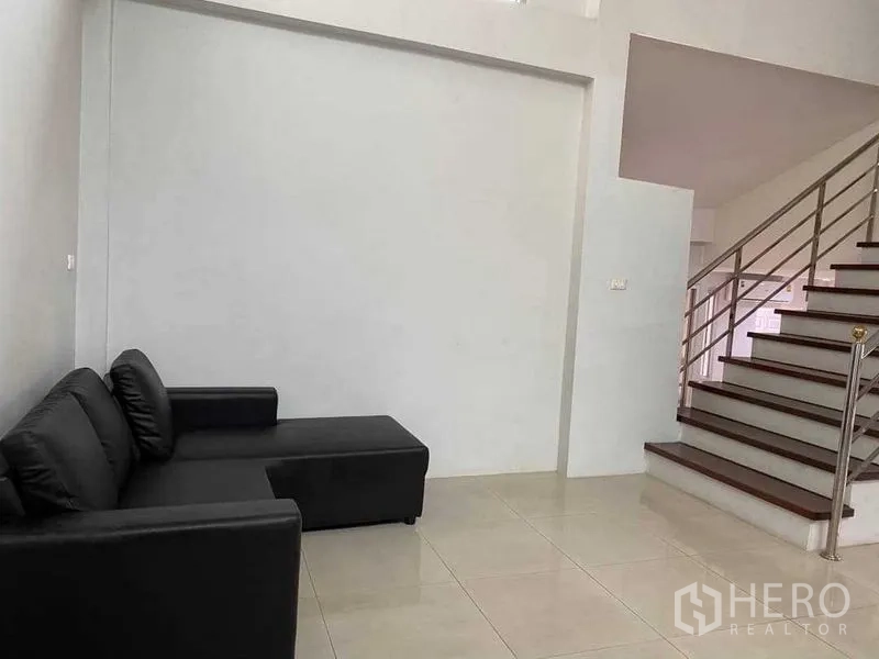 Home Office for rent in Khlong Toei, Bangkok - Small sitting area with black L-shaped sofa beside the staircase.
