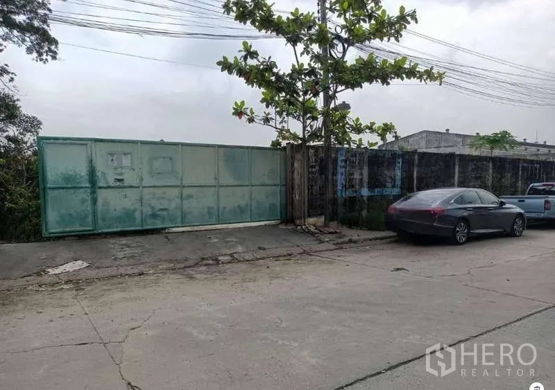 地 出租在Lat Krabang, Bangkok - 临街面展示宽幅推拉铁门，地块入口旁停有车辆。