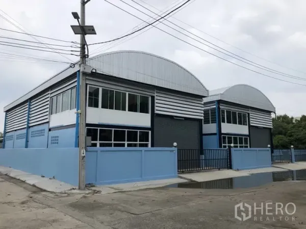 Factory for rent or sale in Bang Bua Thong, Nonthaburi - Row of new warehouse factory units with curved roofs and gated frontage on a quiet street.