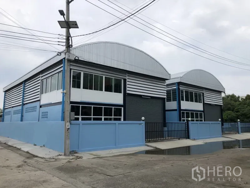 Factory for rent or sale in Bang Bua Thong, Nonthaburi - Row of new warehouse factory units with curved roofs and gated frontage on a quiet street.