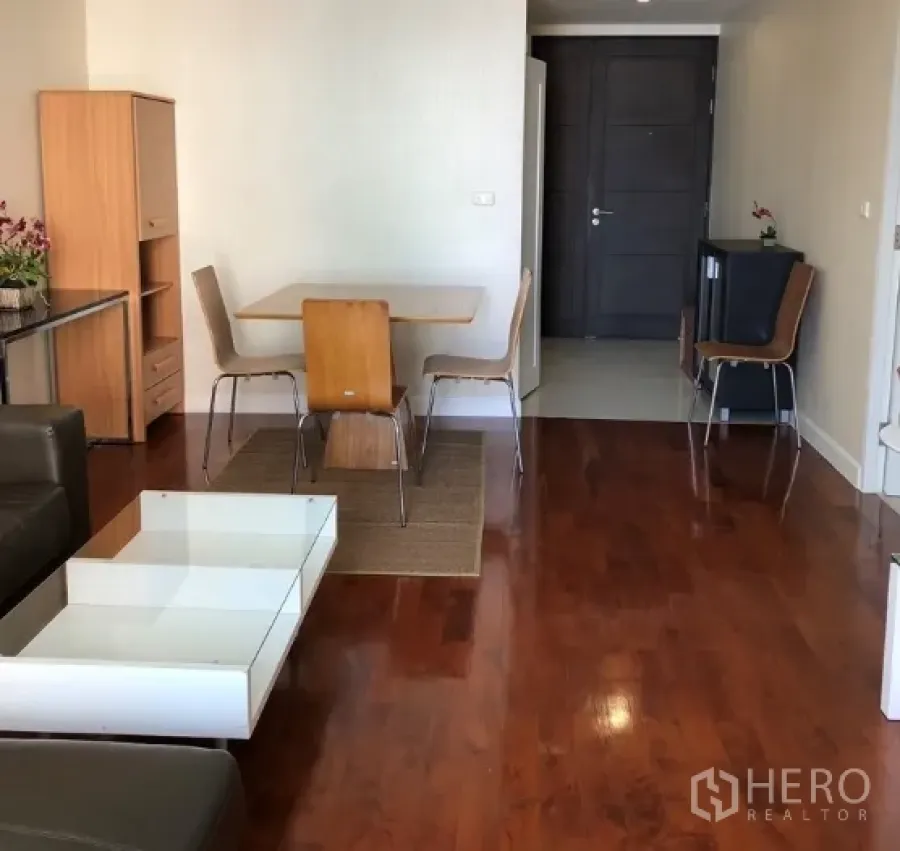 Condominium for rent or sale in Khlong Toei, Bangkok - Open-plan living and dining area with hardwood floors, a wooden table for four, and entryway.